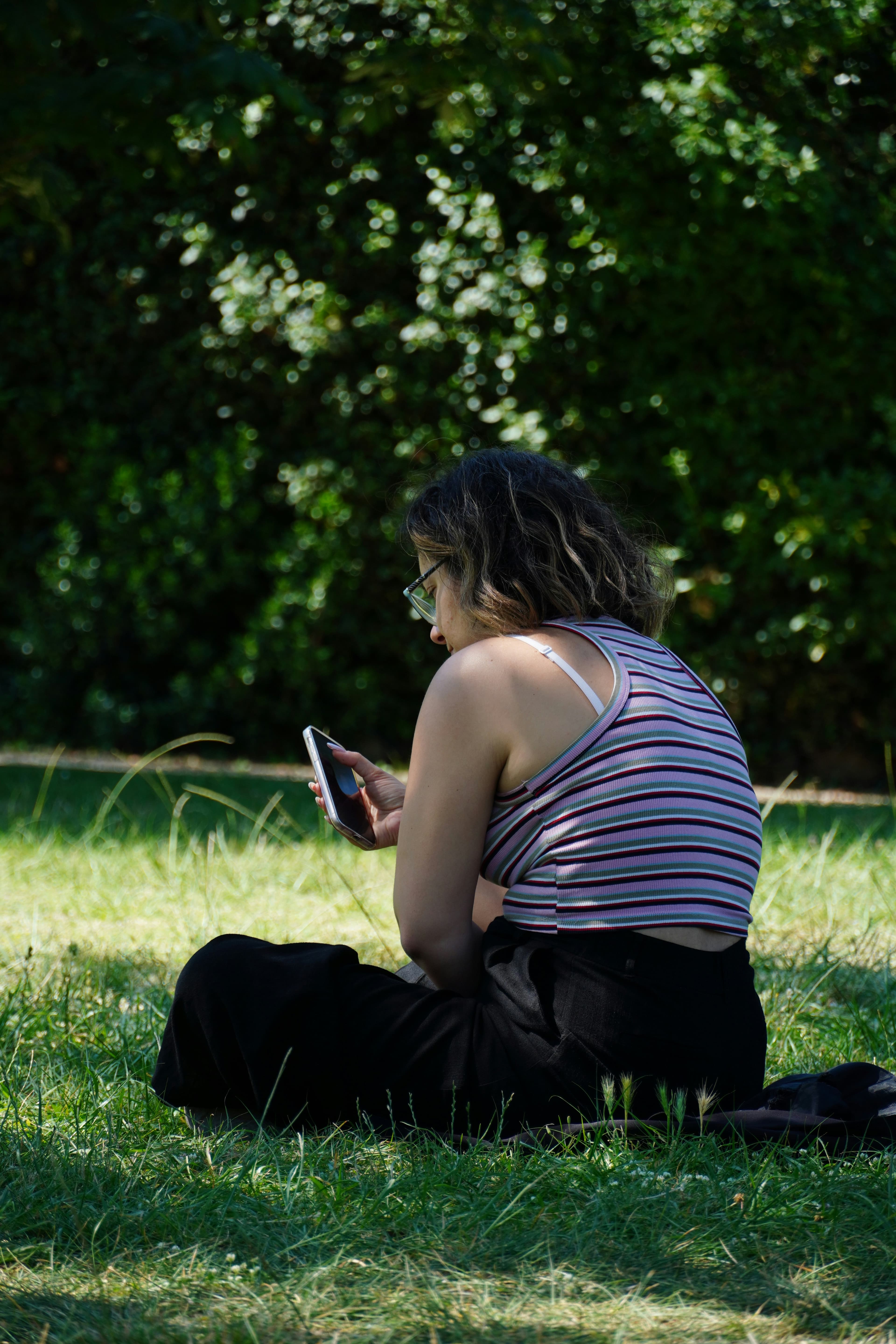 Person sitting in grass using a phone under trees